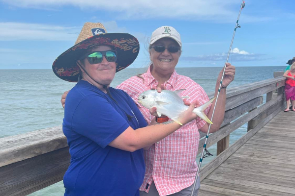 two people holding a fish standing on a pier
