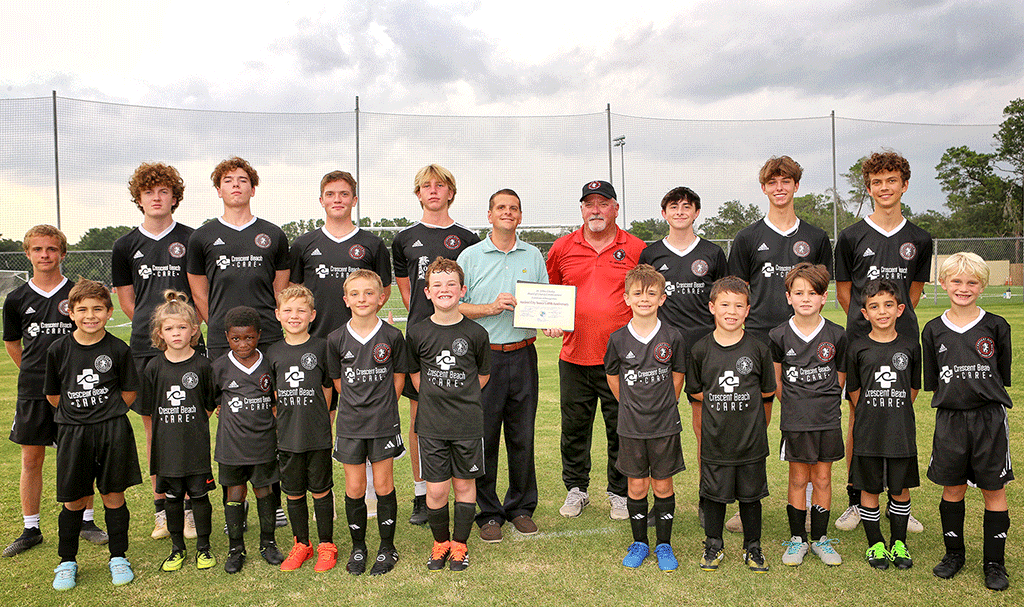 Commissioner Alaimo standing with the Ancient City Soccer team while holding his certificate of recognition