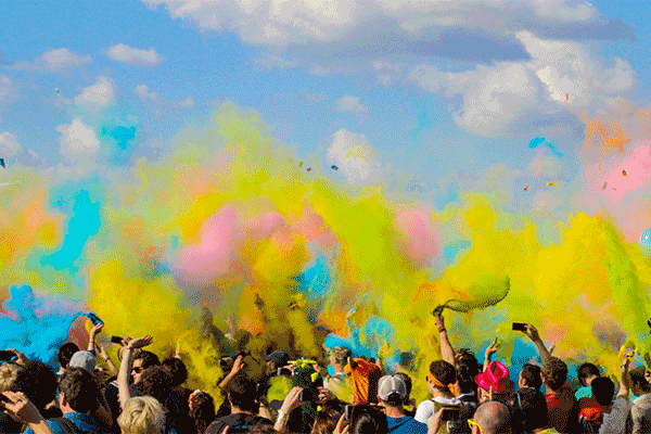 A crowd of people throwing colored powder in the air outdoors.