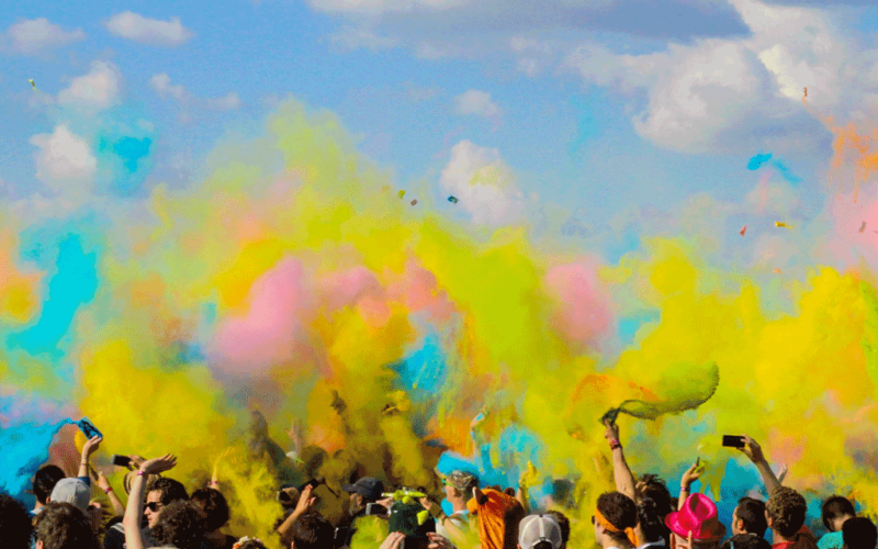 A crowd of people throwing colored powder in the air outdoors.