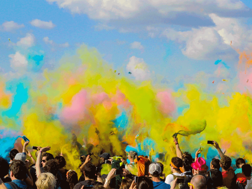 A crowd of people throwing colored powder in the air outdoors.