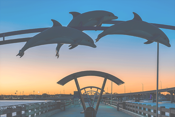 dolphin sculpture over boardwalk with sunset