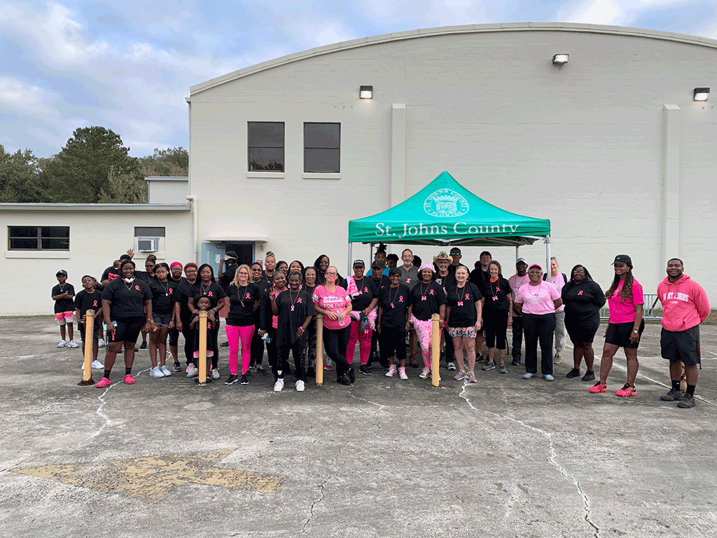 A large group of people in pink and black walking attire outside by a tent.