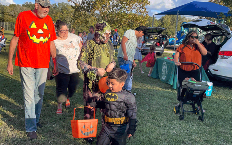 Children and adults go trunk-or-treating in a public park.