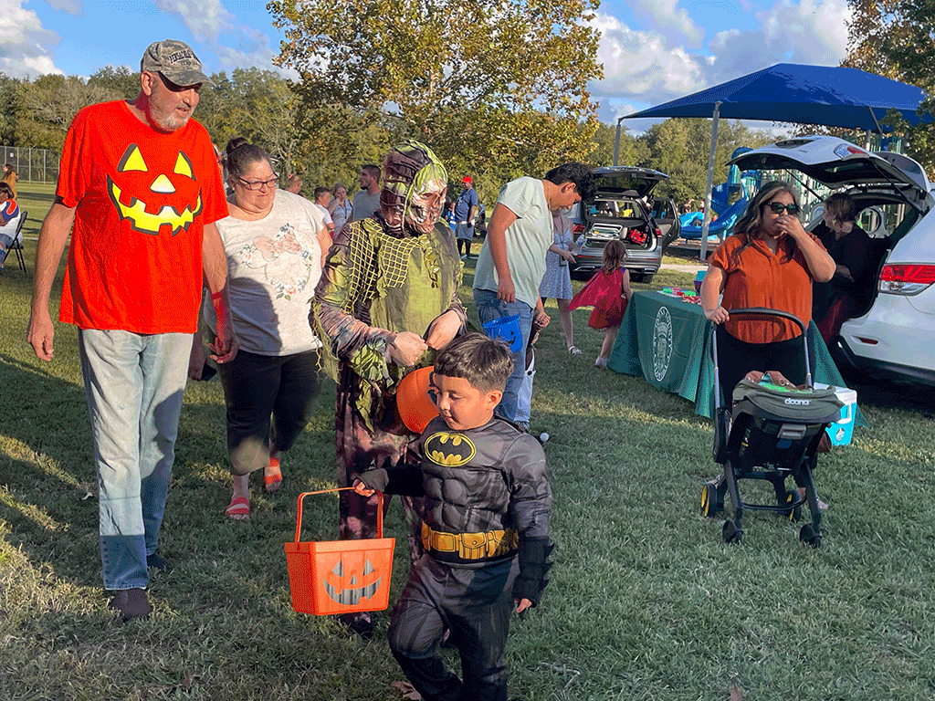 Children and adults go trunk-or-treating in a public park.