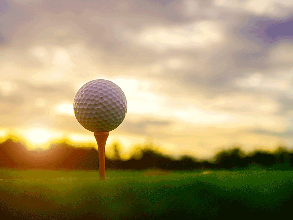 A golf ball teed up on green grass in front of a sunset.