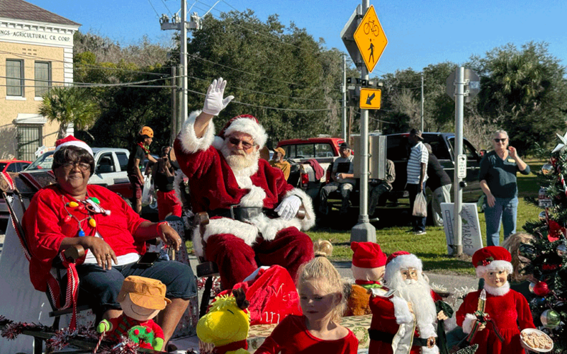 Santa Claus and Mrs. Claus waving to people from a parade float rolling down the street