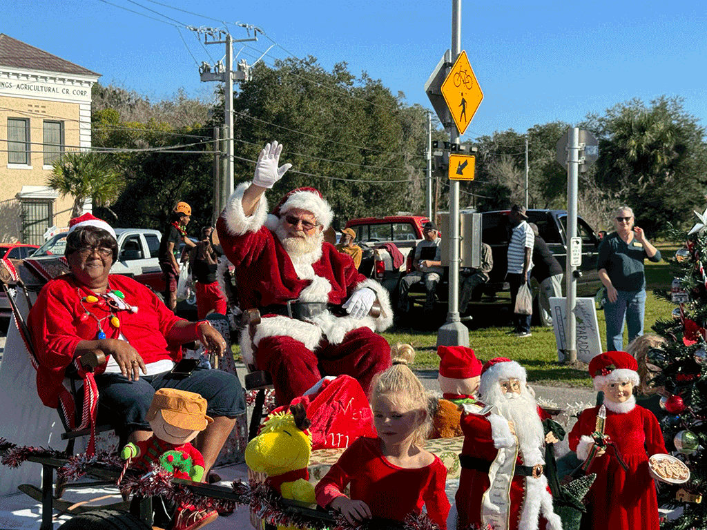 Santa Claus and Mrs. Claus waving to people from a parade float rolling down the street