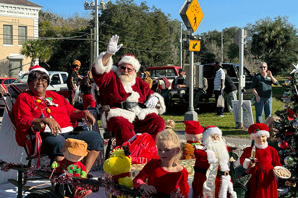 Santa Claus and Mrs. Claus waving to people from a parade float rolling down the street