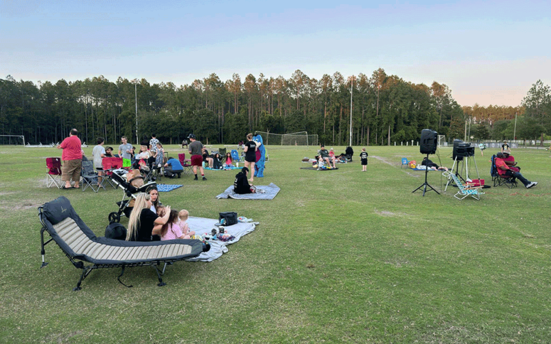 A crowd of families on blankets and lawn chairs on a grassy sports field