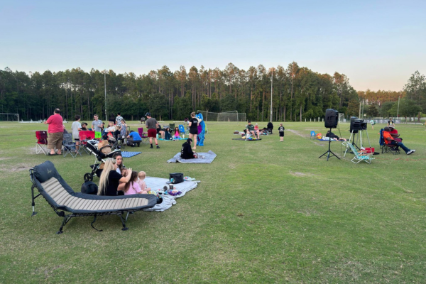 A crowd of families on blankets and lawn chairs on a grassy sports field