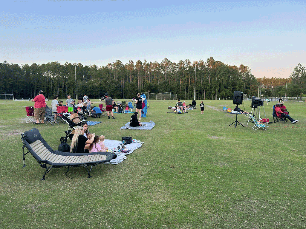 A crowd of families on blankets and lawn chairs on a grassy sports field