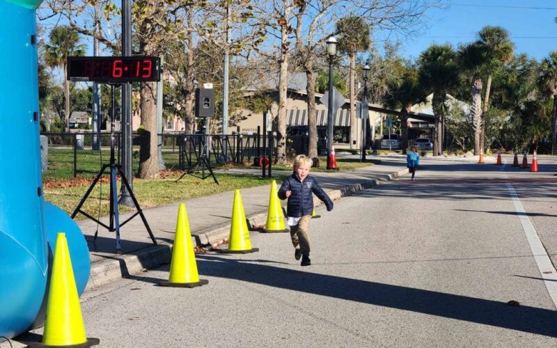 Two small children sprinting toward a finish line on a closed-off street.