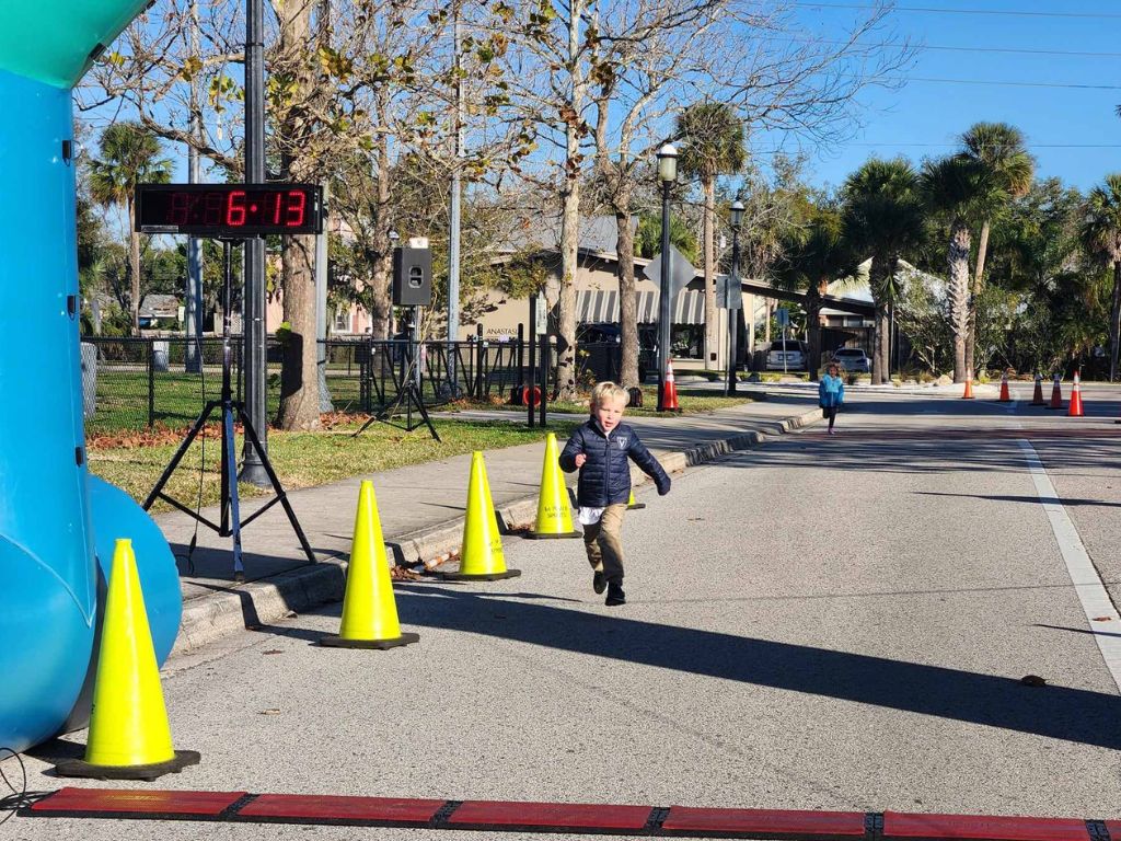 Two small children sprinting toward a finish line on a closed-off street.