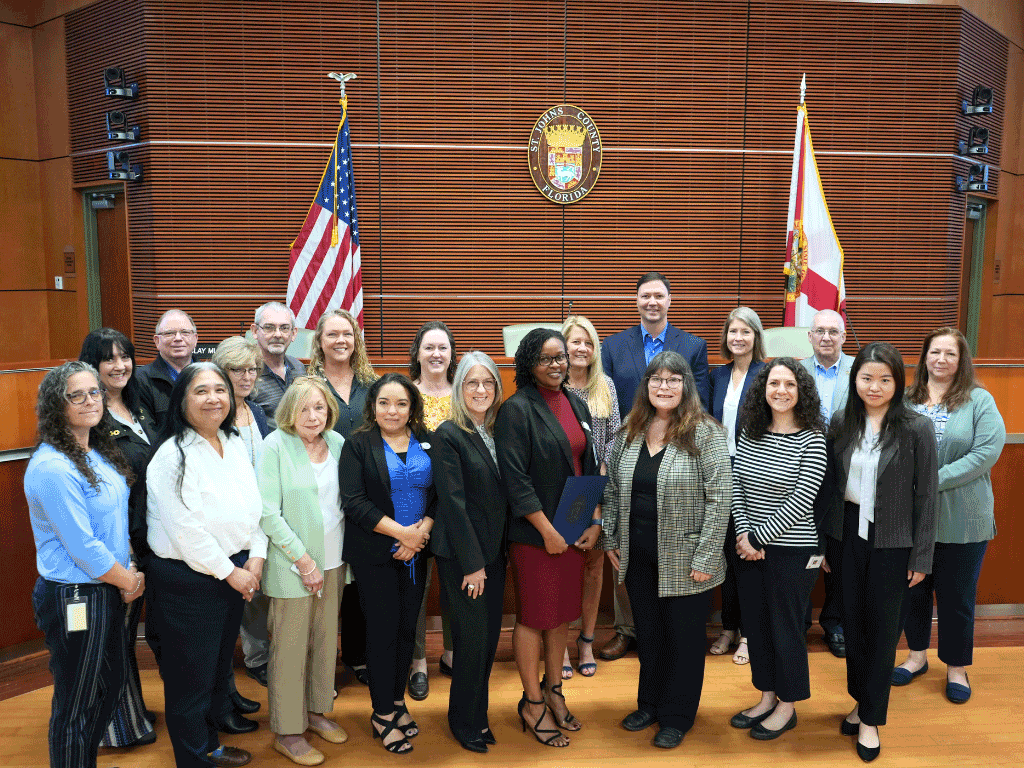 Commissioner Joseph presenting the proclamation on Government Finance Professionals Week with group in front of St. Johns County seal.